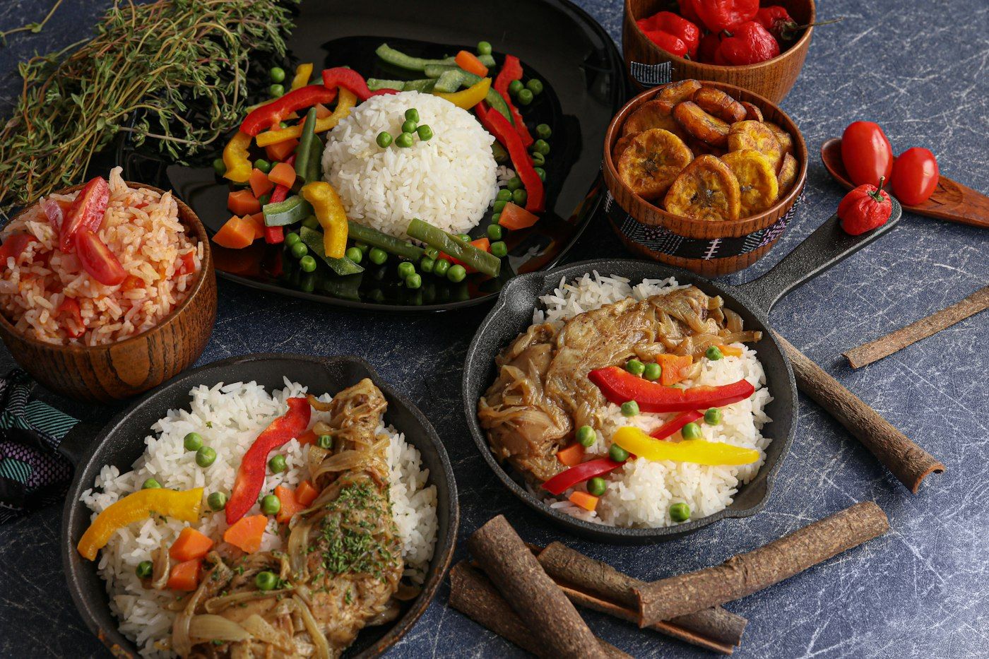 A spread of rice, stews and fried plantain in serving pans